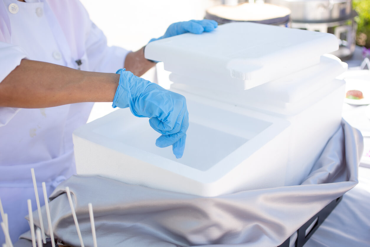 a person wearing blue gloves opens a styrofoam box