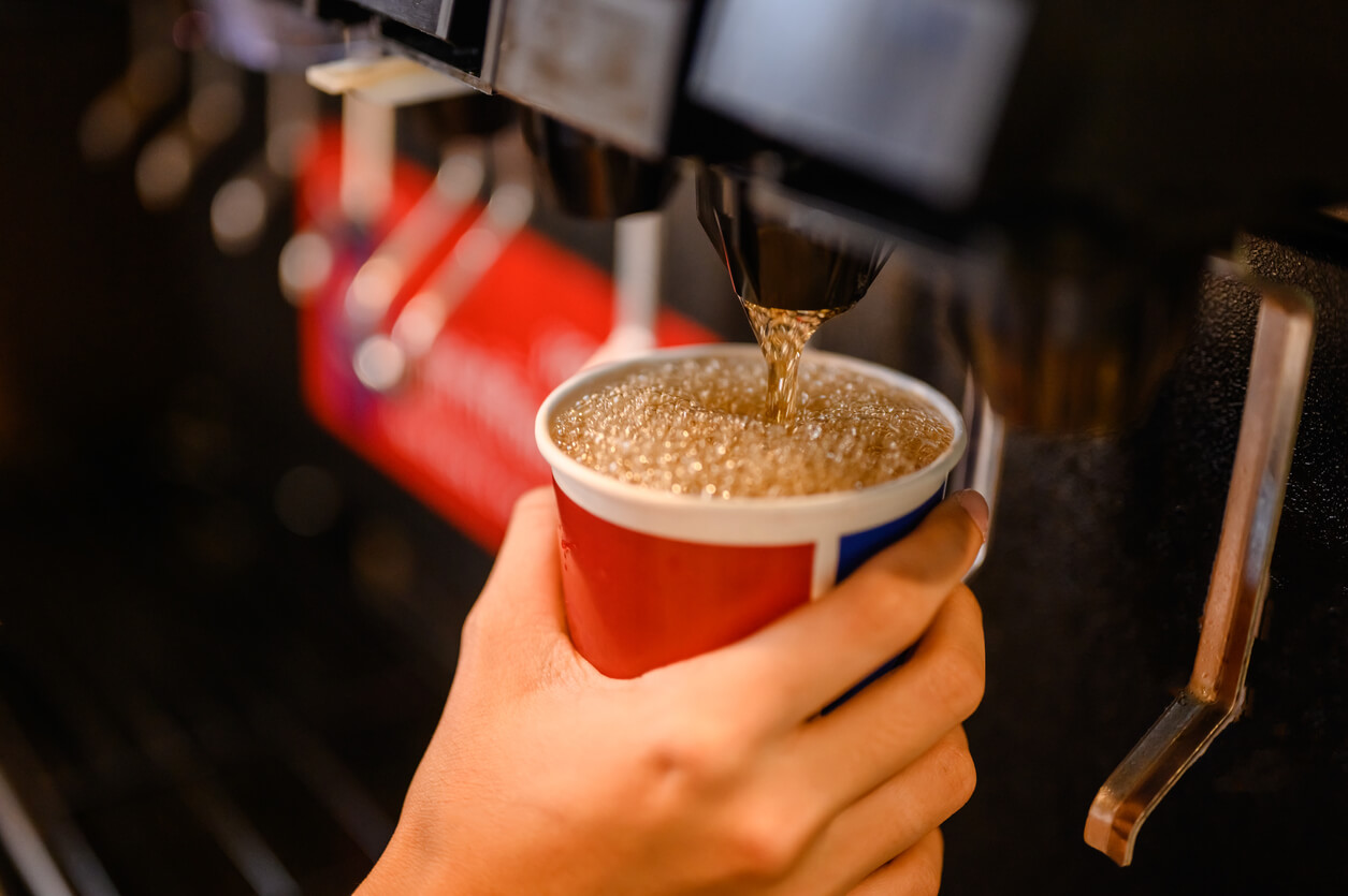 a hand is holding a cup of soda that is being poured into it