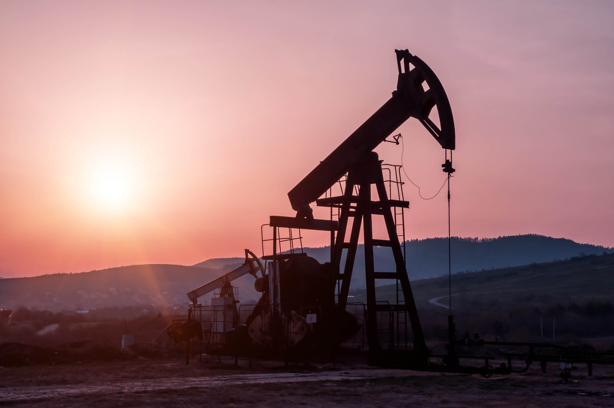 an oil pump is silhouetted against a pink sky at sunset